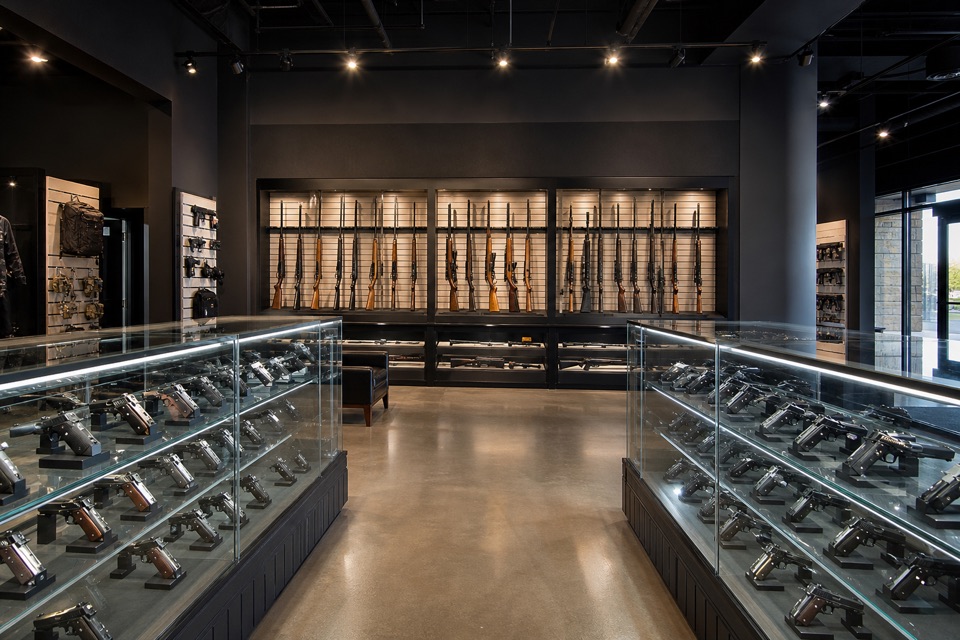 AI-generated illustration of spacious contemporary firearms showroom with charcoal walls, well-lit locked glass handgun cases and secure sporting-rifle displays, polished concrete floor, balanced architectural photograph