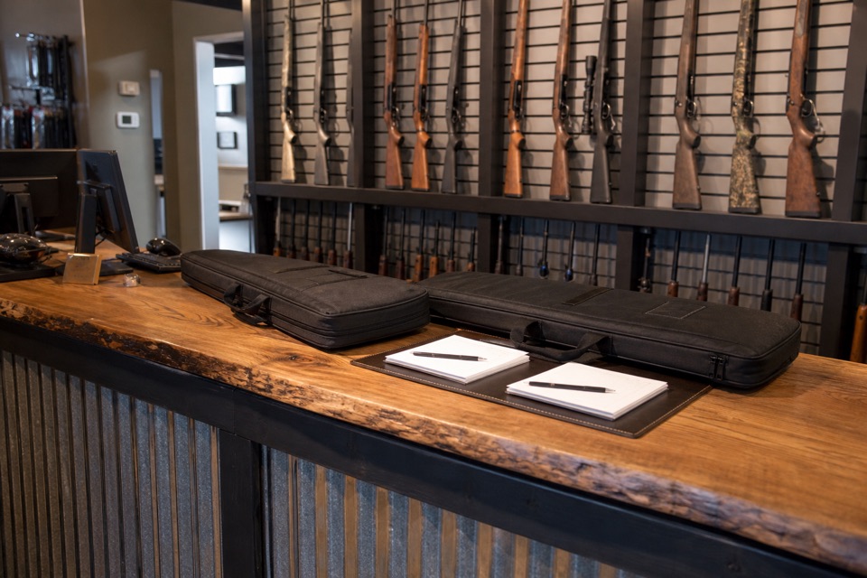 AI-generated illustration of professional FFL dealer pickup desk, two closed padded firearm cases neatly arranged beside blank forms, secure sporting-rifle display wall behind, no transaction details or handling steps